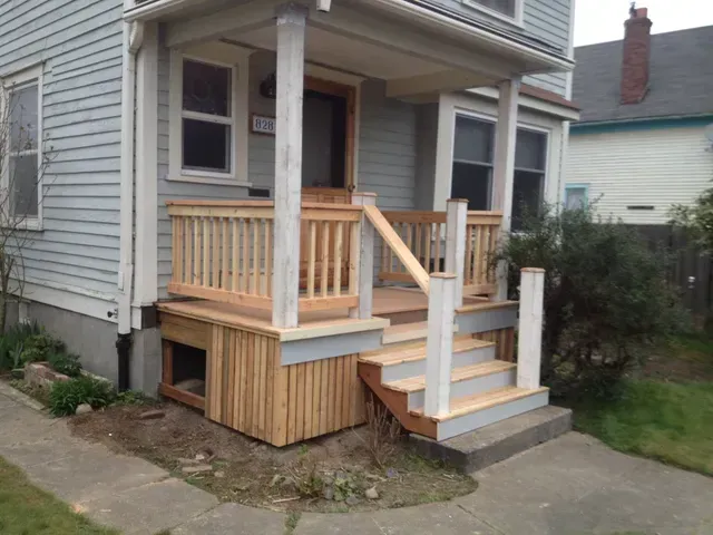 Front porch with wooden accessibility ramp and stairs on a gray house.