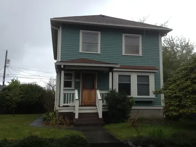 Two-story teal house with white trim and a covered front porch on a cloudy day