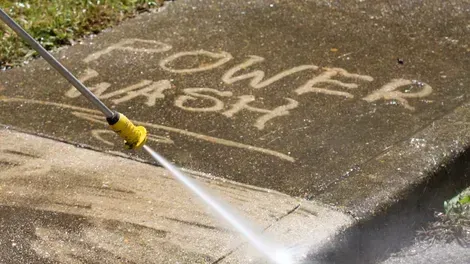 Person pressure-washing sidewalk graffiti reading “Power to the…”