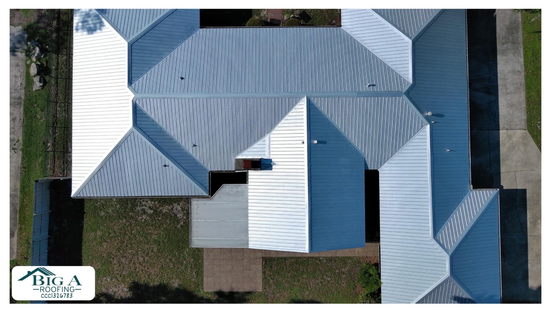 An aerial view of a silver metal residential roof with multiple gables and slopes, featuring a Big A Roofing company logo.