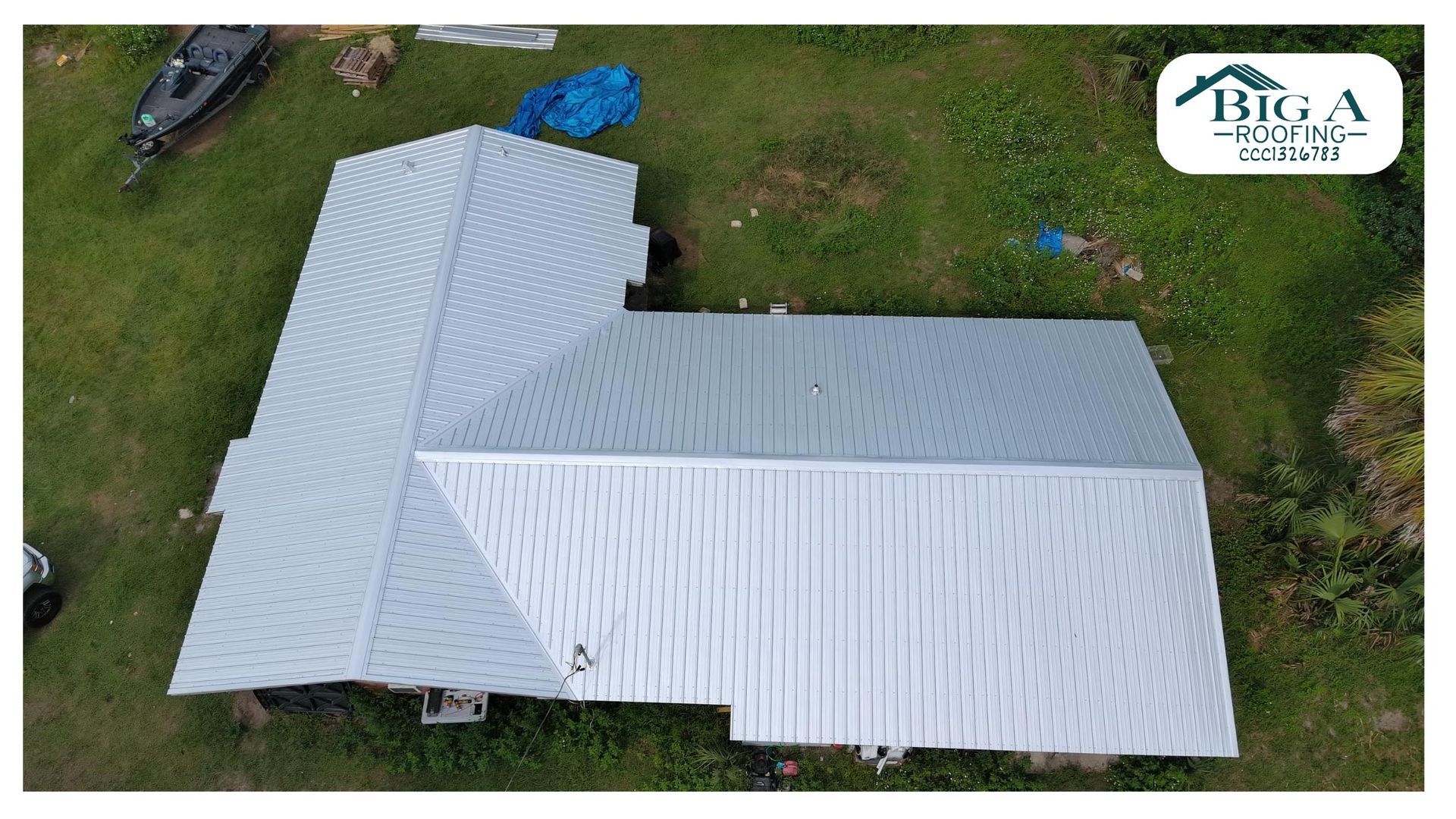 Aerial view of a gray metal roof on an L-shaped house in a grassy yard, with a Big A Roofing logo in the corner.