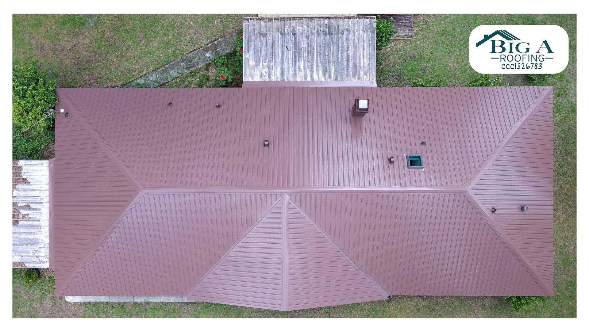 An aerial view of a rectangular, dark brown metal roof with a chimney and a small deck attached to the side.