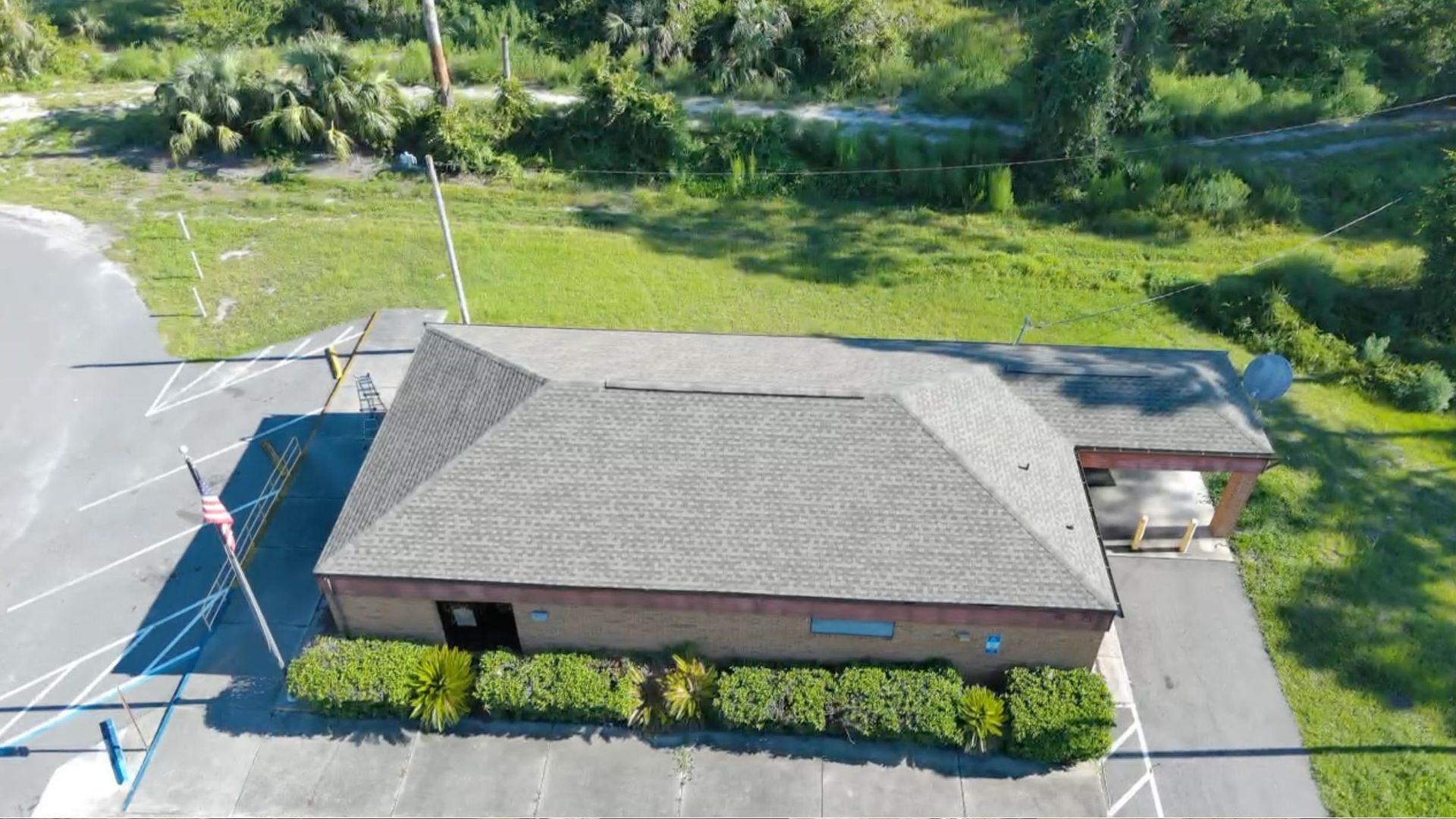 Aerial view of a rectangular, single-story brick commercial building with a gray roof and parking lot on a sunny day.