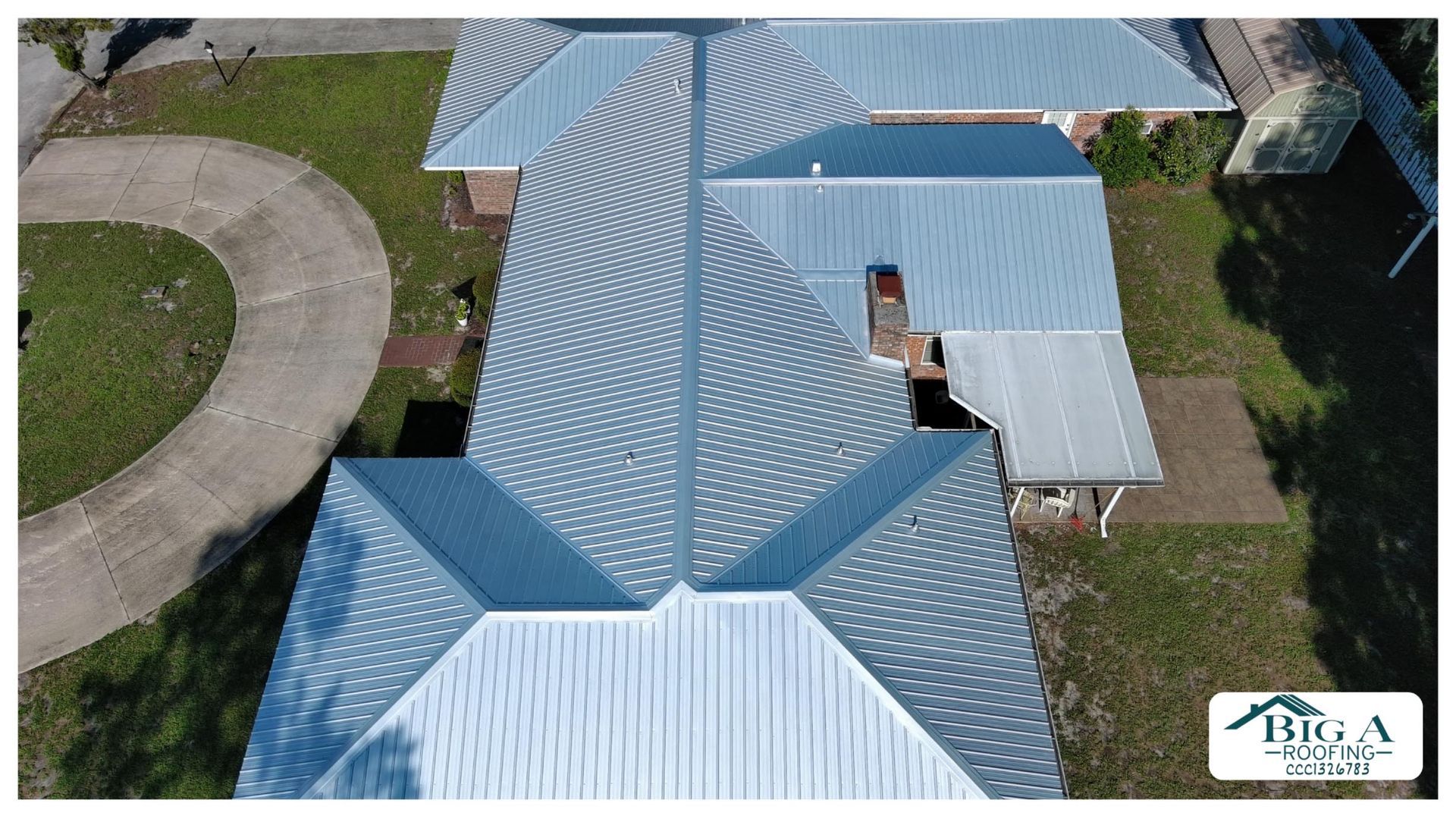 An aerial view of a light-colored metal roof on a residential home, featuring multiple peaks and a chimney.