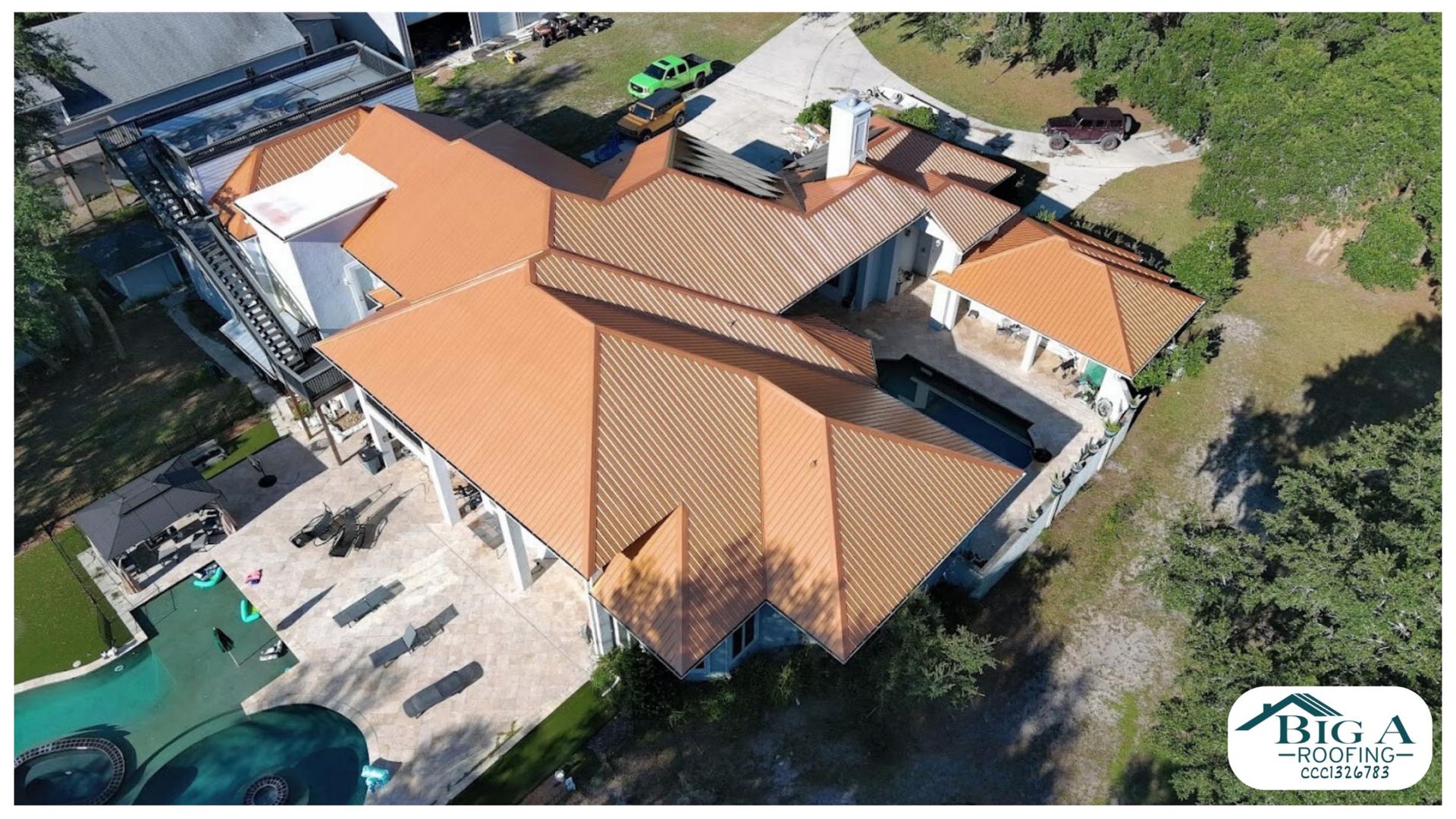 Aerial view of a large residential house with a terracotta-colored tile roof, featuring a pool and patio area.