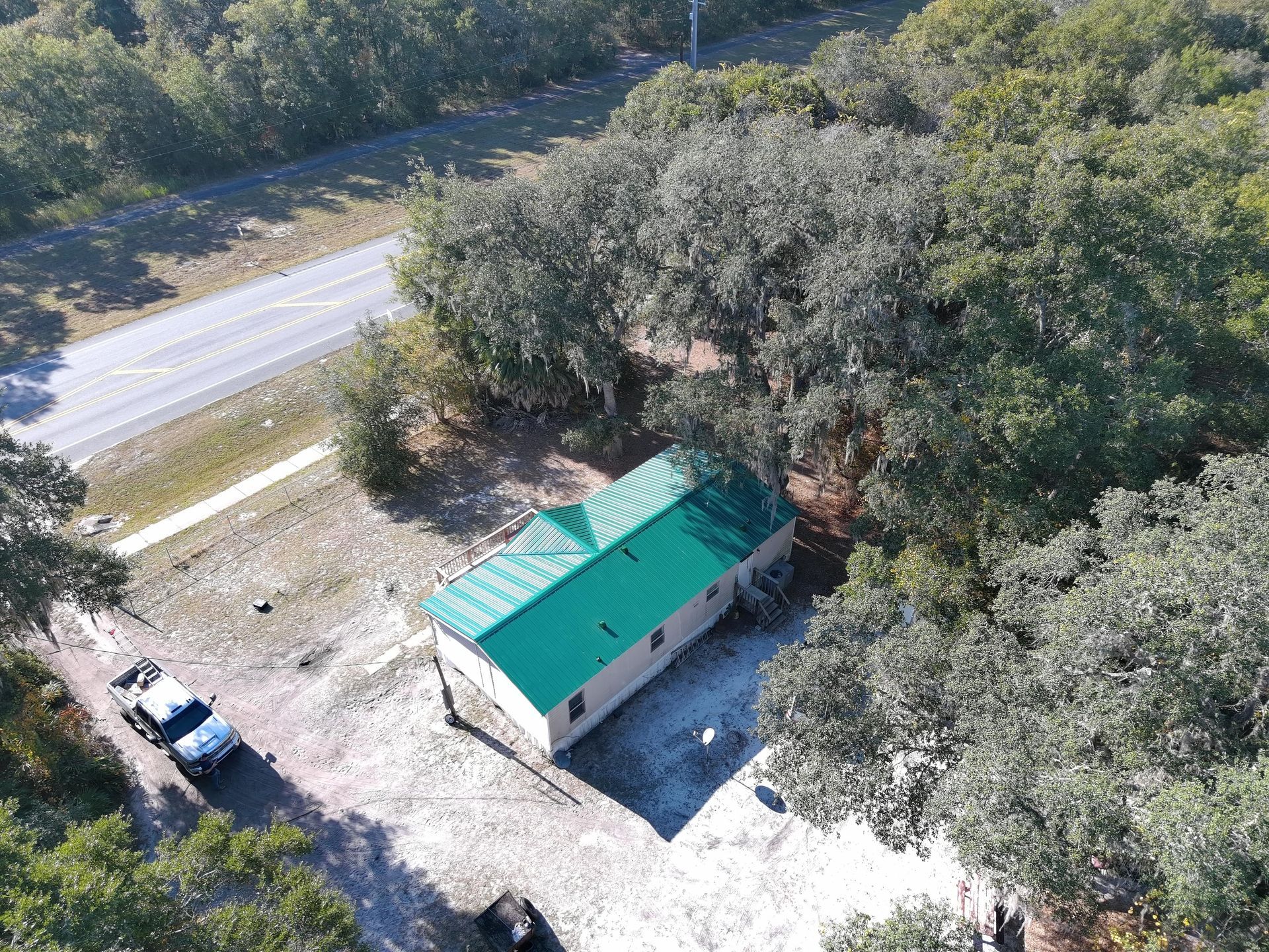 An aerial view of a small building with a bright green roof situated on a gravel lot next to a road and trees.