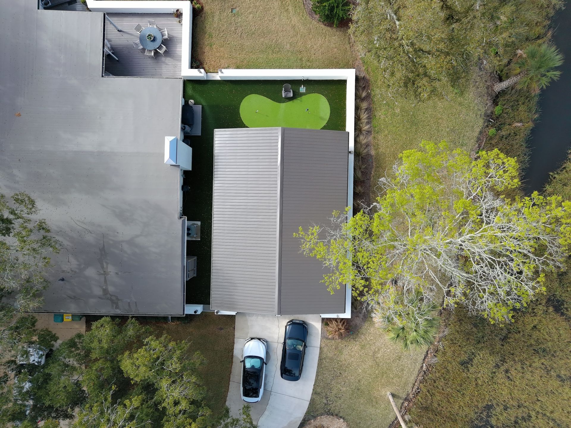 Aerial view of a home with a two-tone roof, a small putting green, and two cars parked in a concrete driveway.