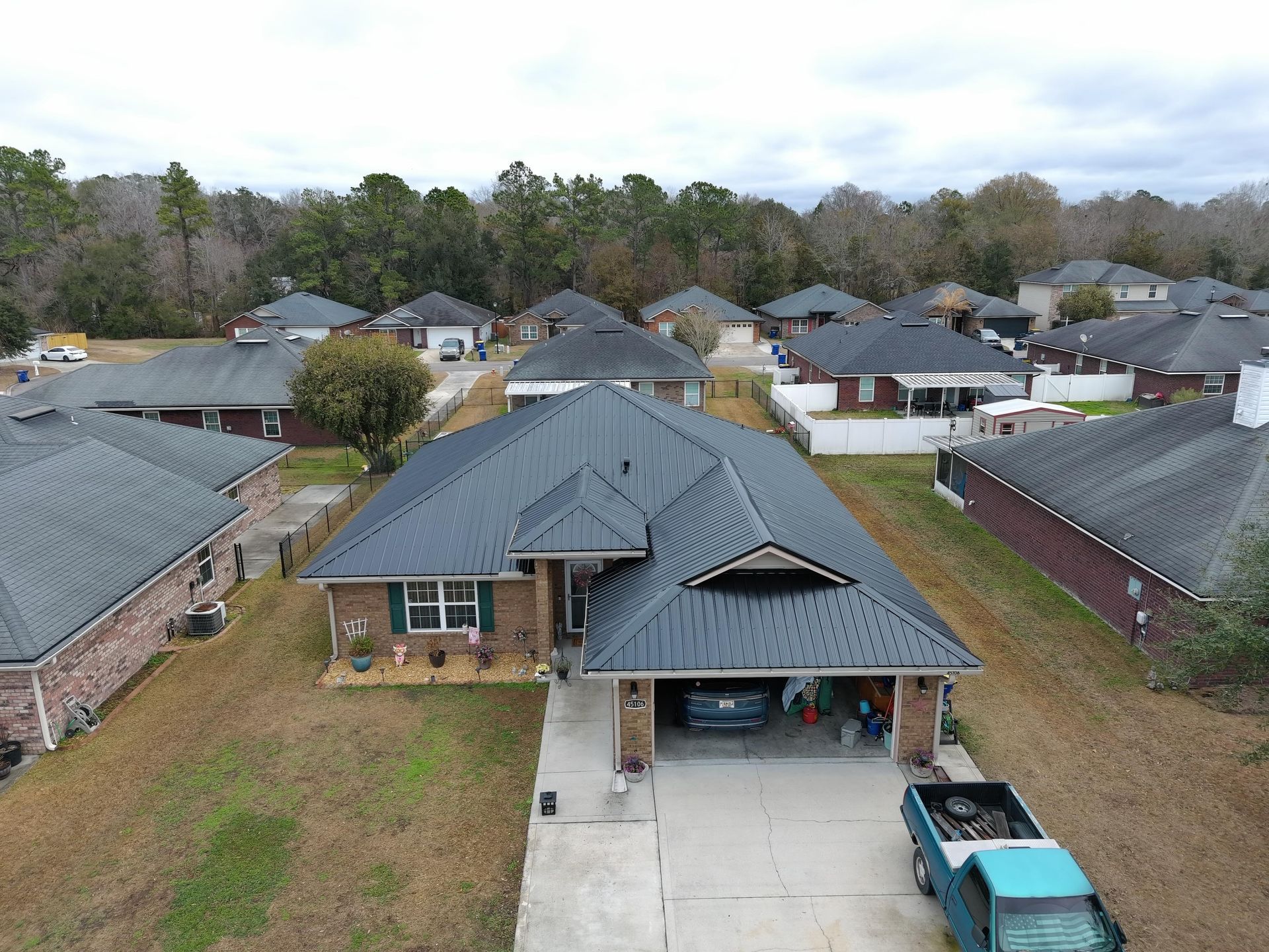Aerial view of a residential brick house with a dark metal roof and a turquoise pickup truck parked in the driveway.