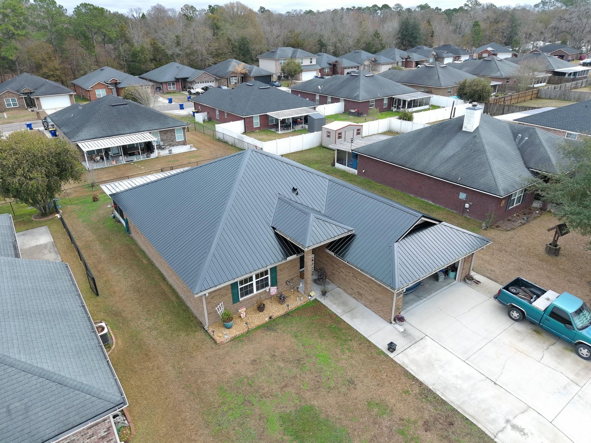 Aerial view of a residential neighborhood with brick houses, dark gray roofs, and a turquoise truck in a driveway.