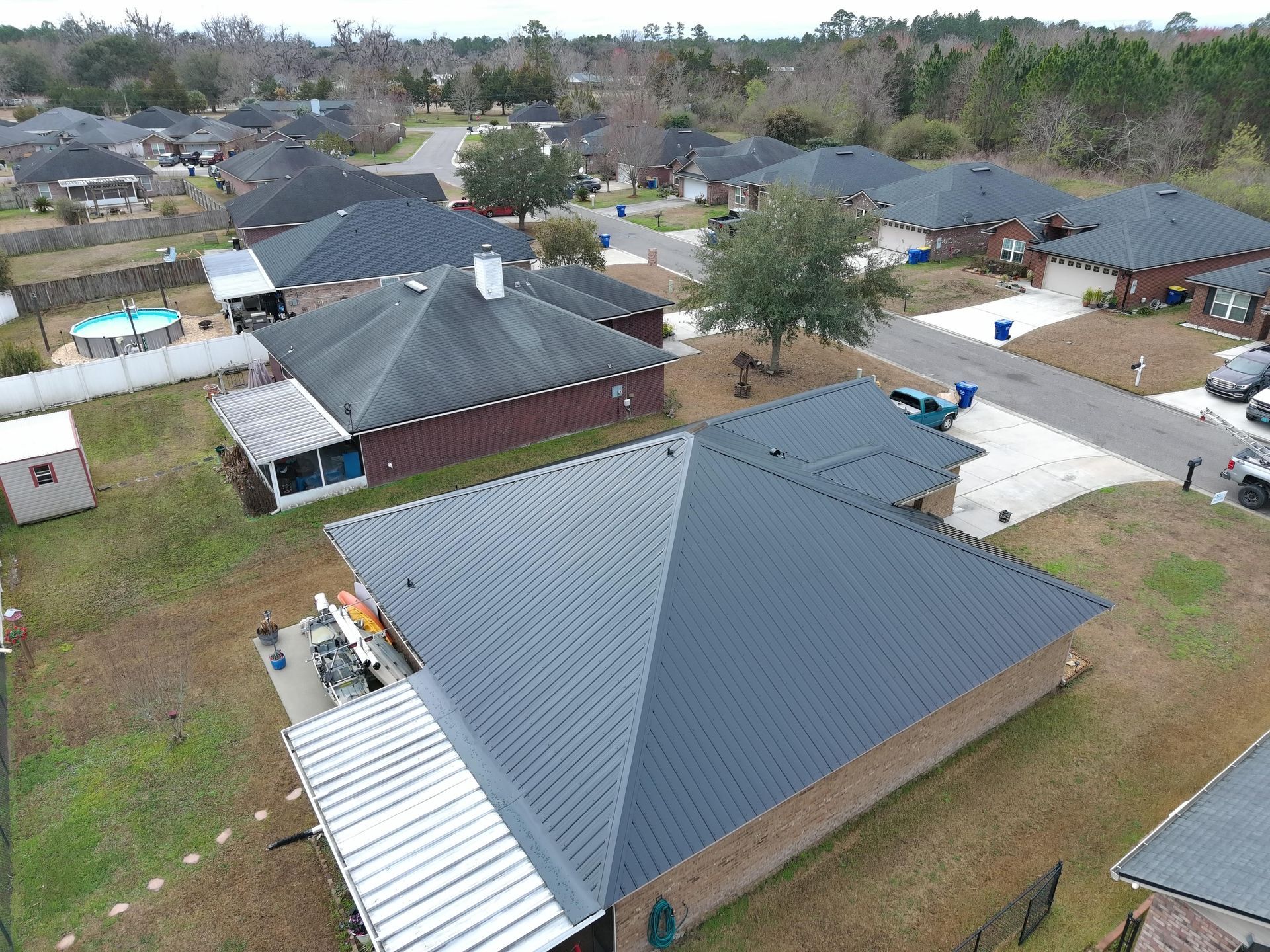 An aerial view of a suburban neighborhood showing rooftops of various homes, a swimming pool, and tree-lined streets.