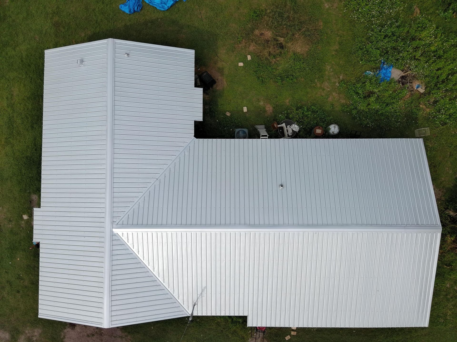 An aerial view of an L-shaped building with a corrugated silver metal roof, situated on a grassy plot.