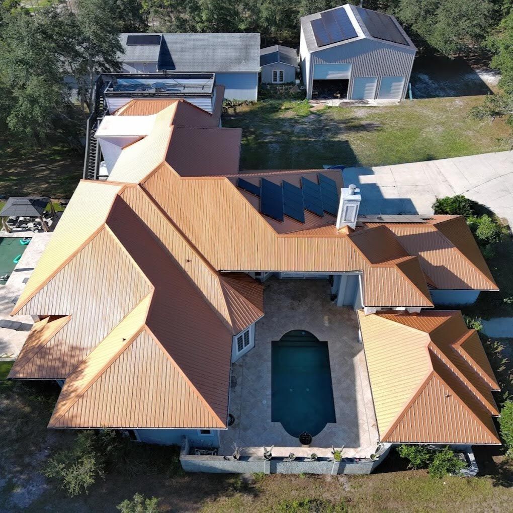 An aerial view of a large residential property with a copper-colored metal roof, swimming pool, and a detached garage.
