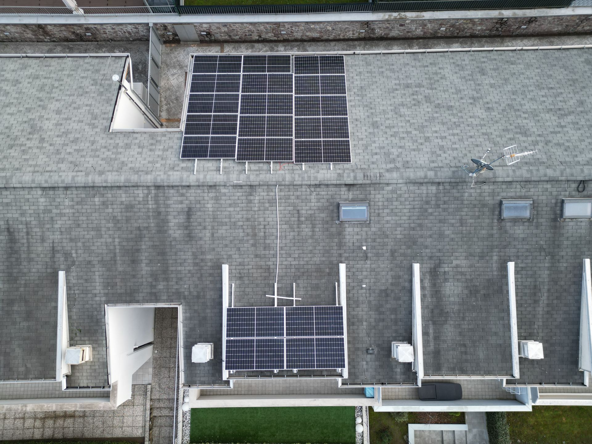 Vista aerea di un tetto piano con pannelli solari, unità di ventilazione e una struttura architettonica bianca.