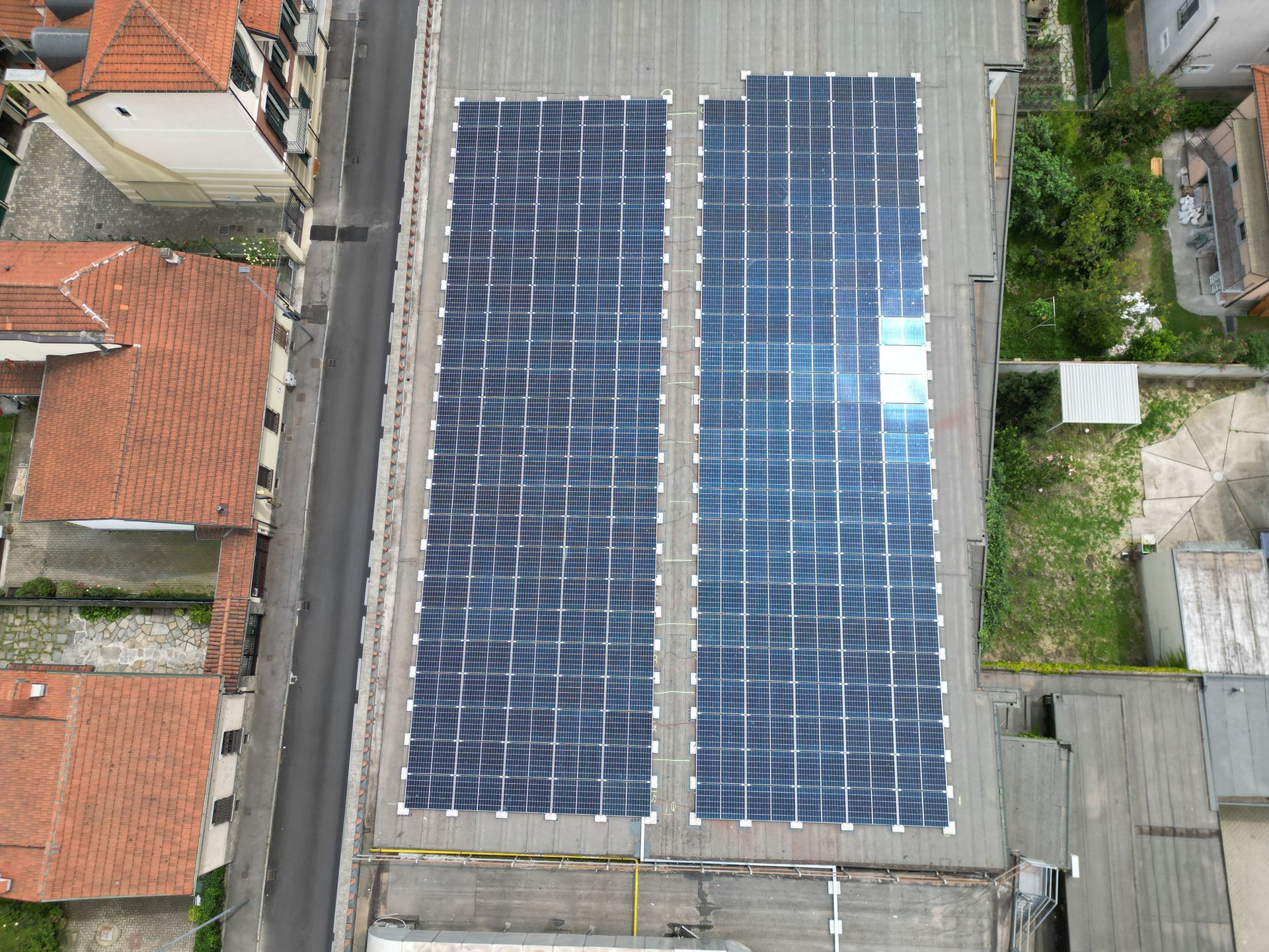 Vista dall'alto di un tetto coperto da due grandi pannelli solari. Sono visibili gli edifici adiacenti con i tetti arancioni.