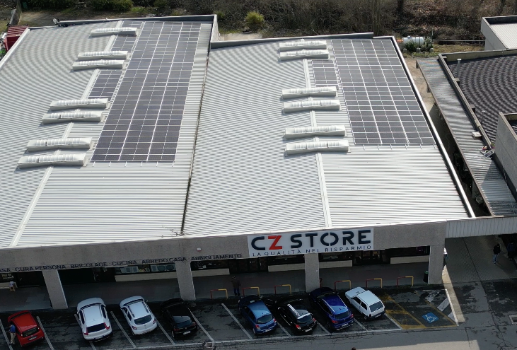 Negozio CZ con pannelli solari sul tetto; auto parcheggiate di fronte.