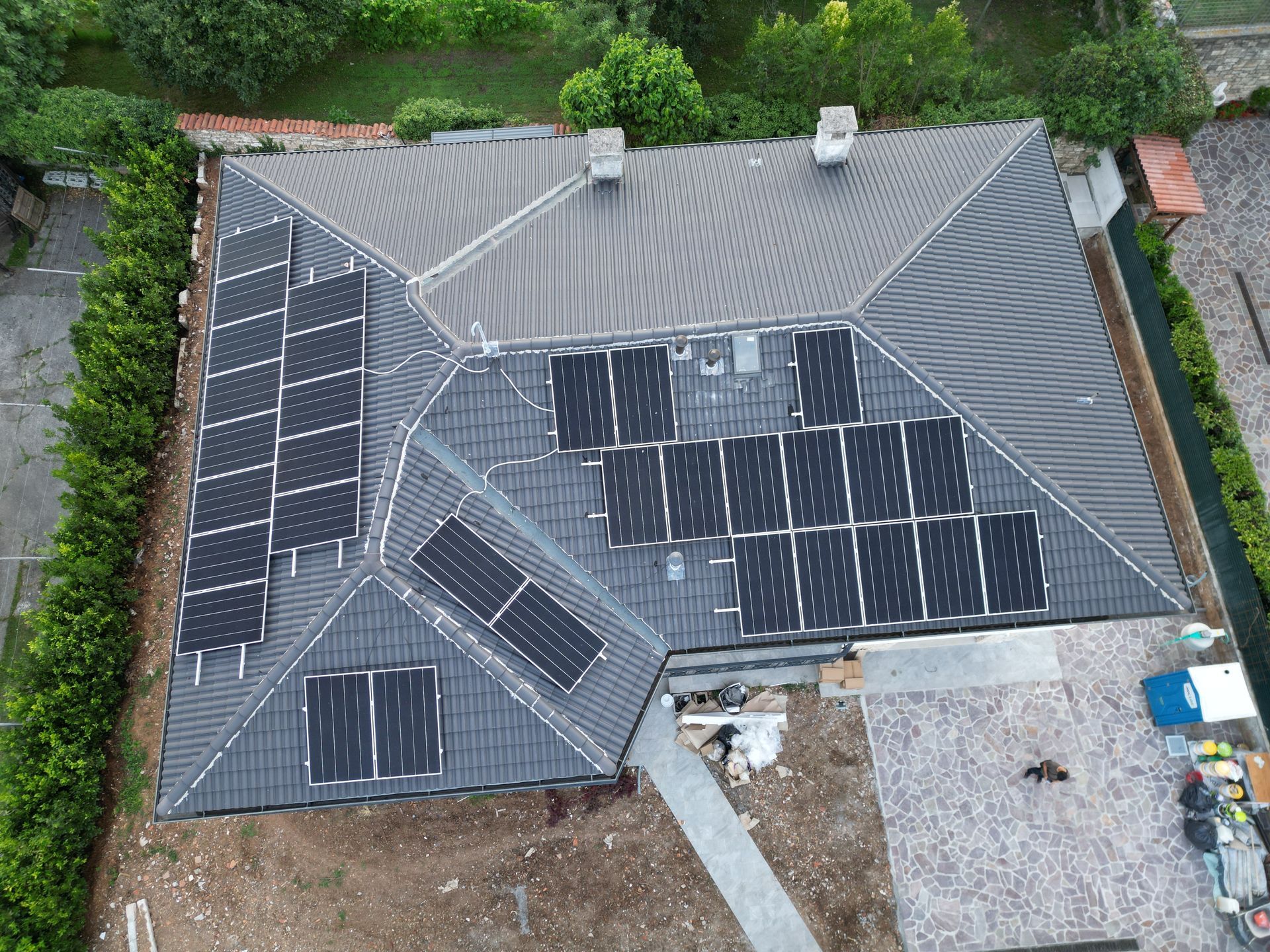Vista aerea di una casa con pannelli solari installati su un tetto grigio, circondata dal verde.