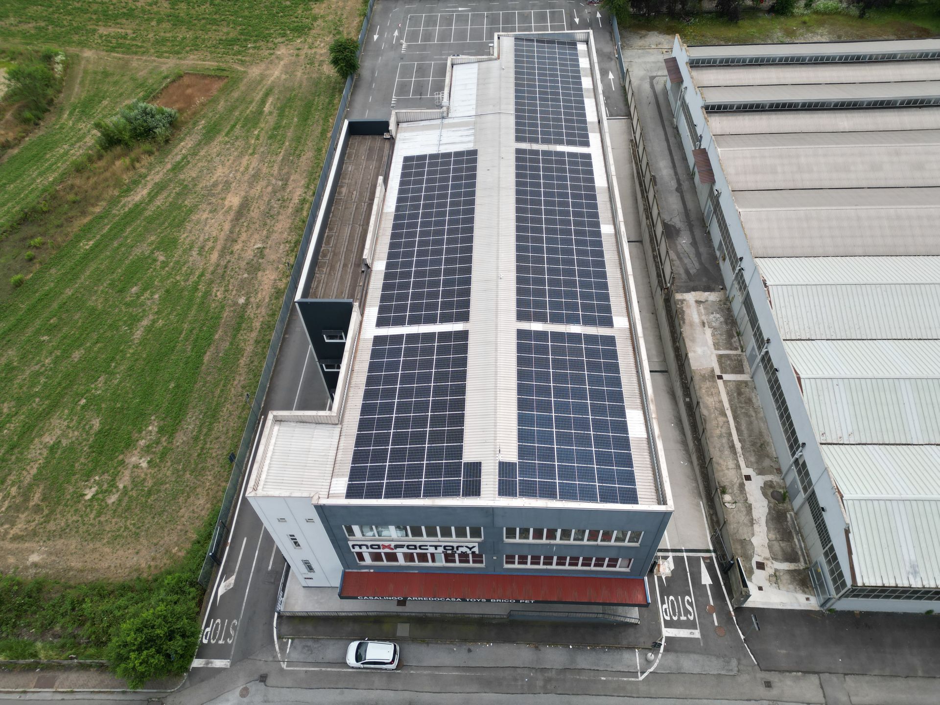 Vista aerea di un edificio con pannelli solari sul tetto. Include parcheggio e prato verde adiacente.
