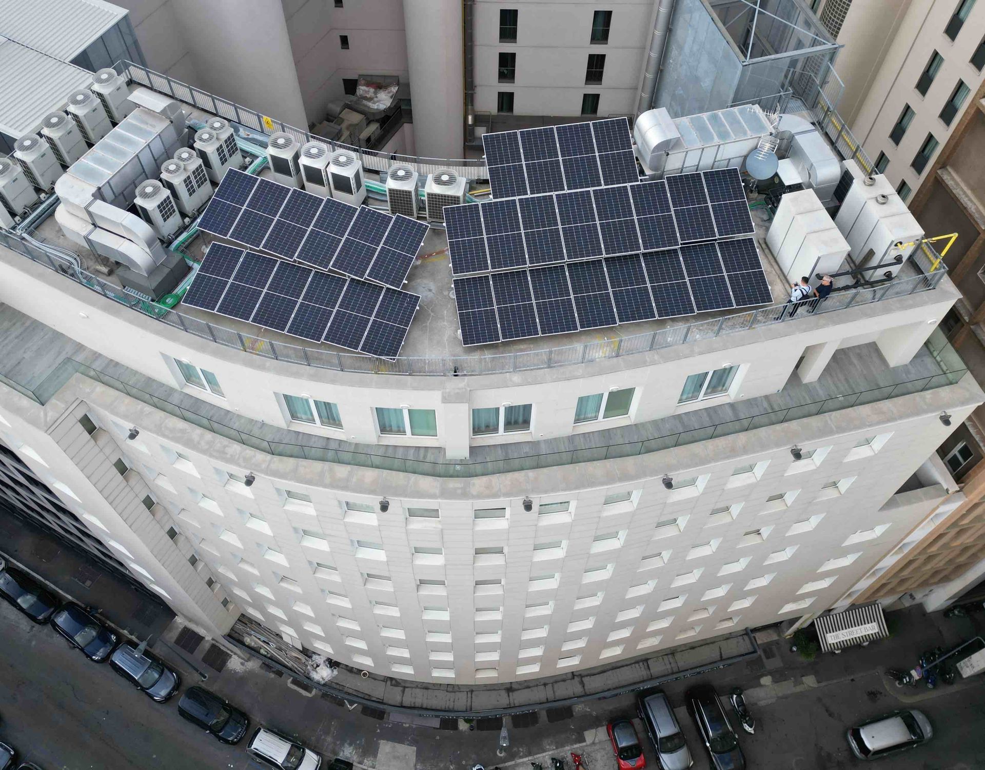 Tetto di un edificio a più piani con pannelli solari. Pannelli neri su un tetto chiaro. Auto parcheggiate sotto.