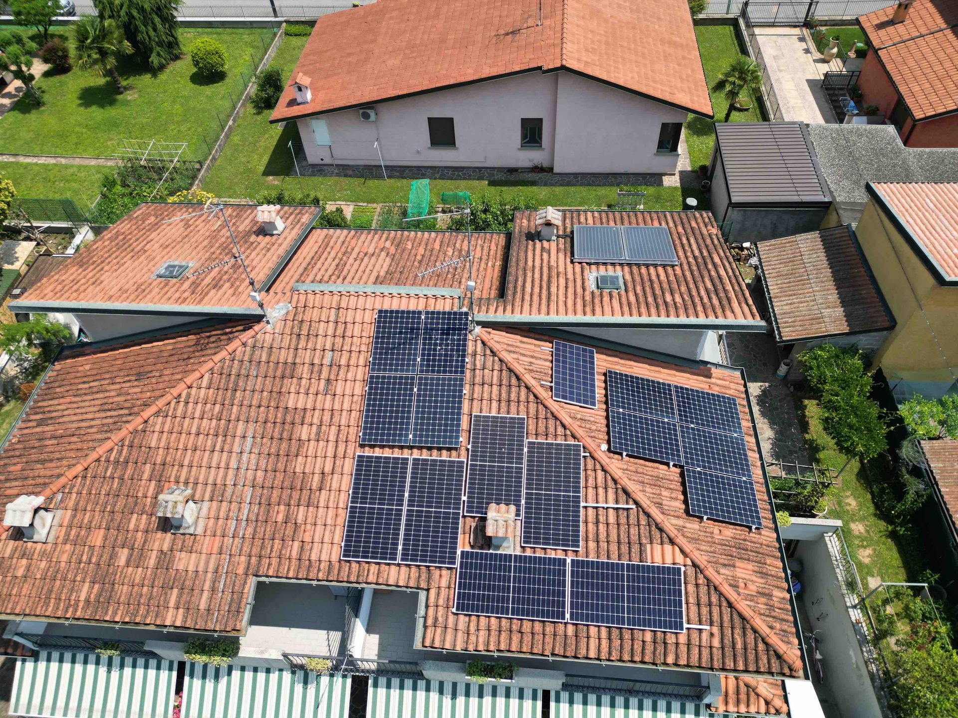 Vista del tetto di una casa con diversi pannelli solari installati, circondata da altre case e vegetazione.