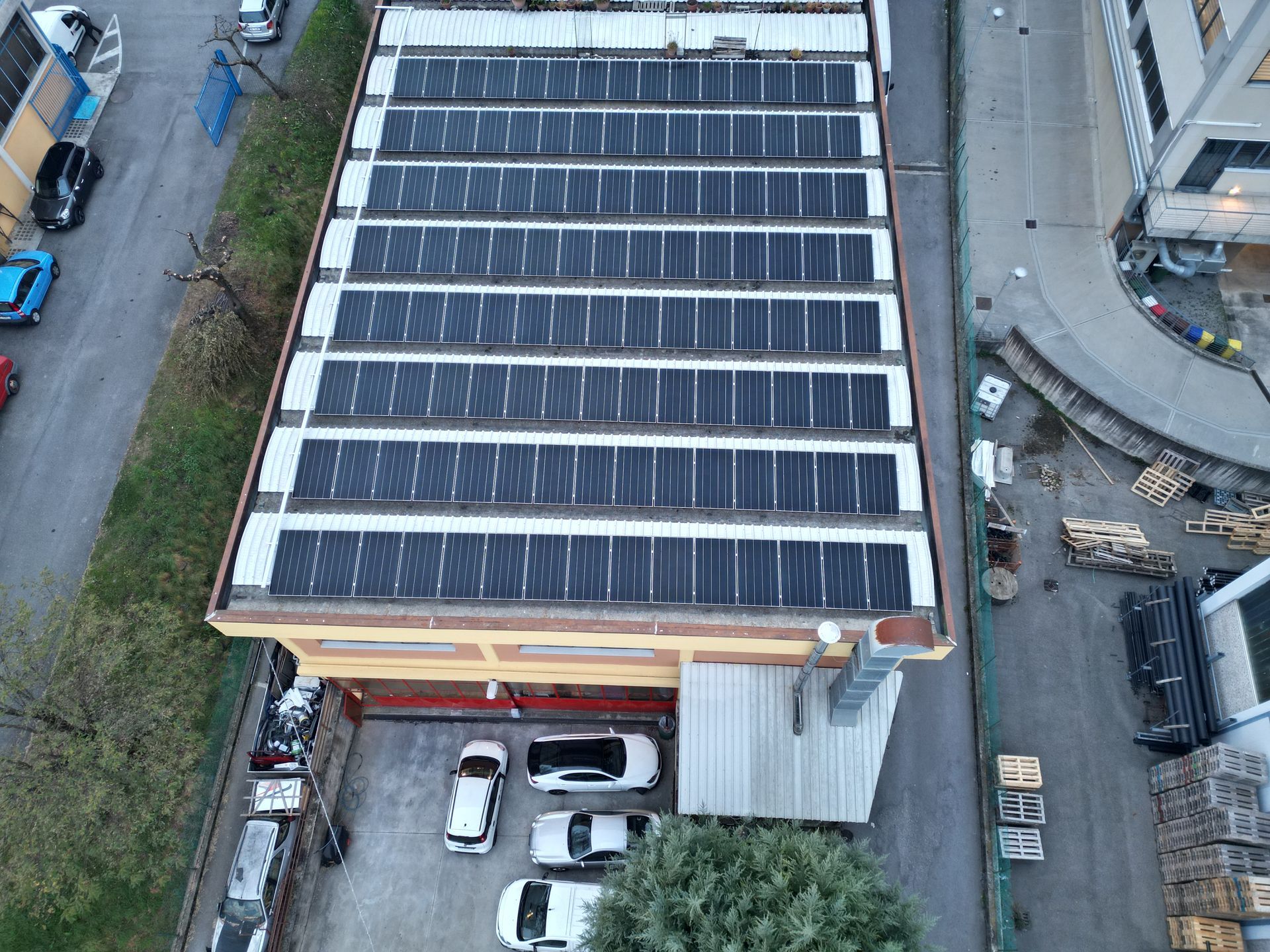 Vista aerea del tetto di un edificio con file di pannelli solari. Auto parcheggiate sotto.