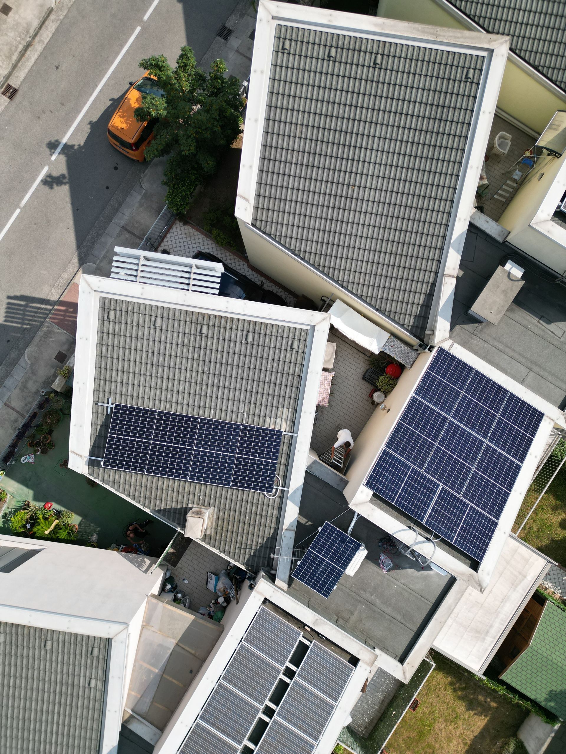 Vista dall'alto dei tetti con pannelli solari; sono visibili una strada e un'auto arancione.