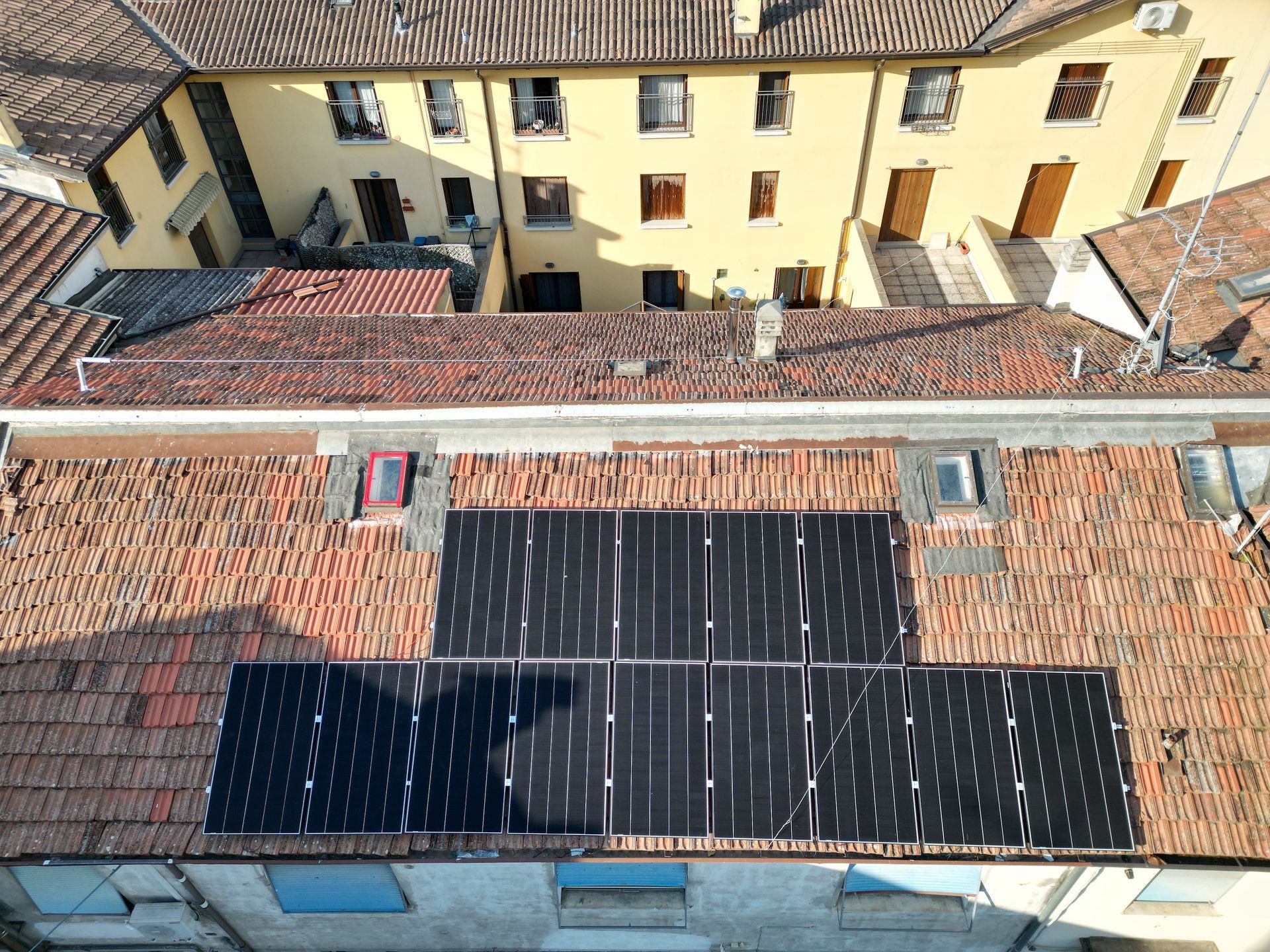 Pannelli solari installati su un tetto di tegole rosse, con un edificio giallo sullo sfondo.