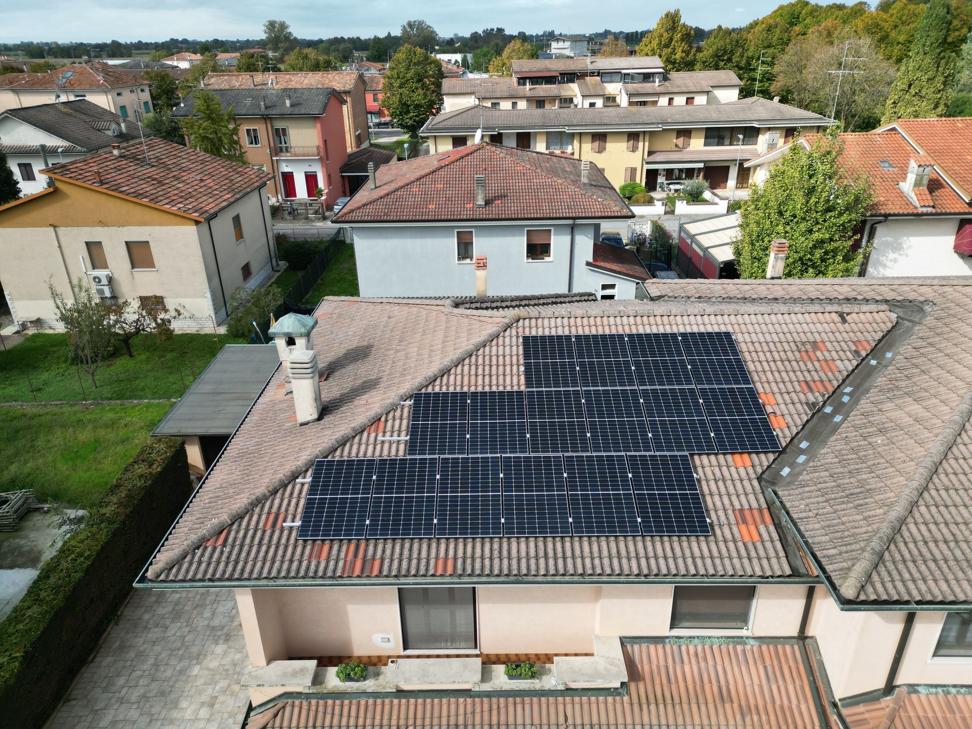 Pannelli solari sul tetto di tegole rosse di una casa in una zona residenziale, circondata da altre case e dal verde.