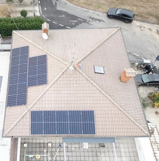 Vista aerea di un tetto di tegole con pannelli solari installati. Un'auto è parcheggiata lì vicino, sulla strada.
