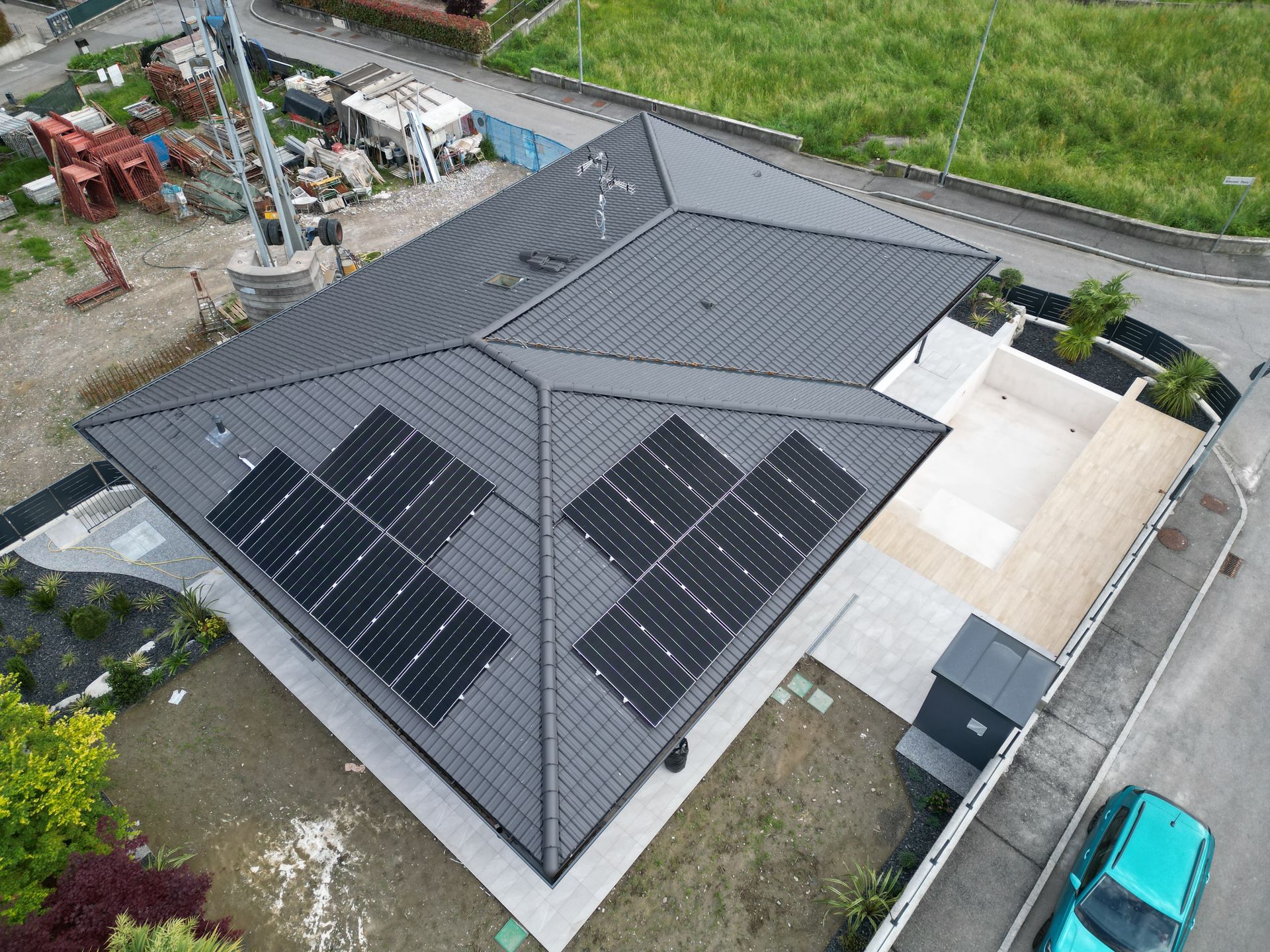 Vista aerea di una casa con tetto grigio scuro e pannelli solari. Un'auto turchese è parcheggiata nelle vicinanze.