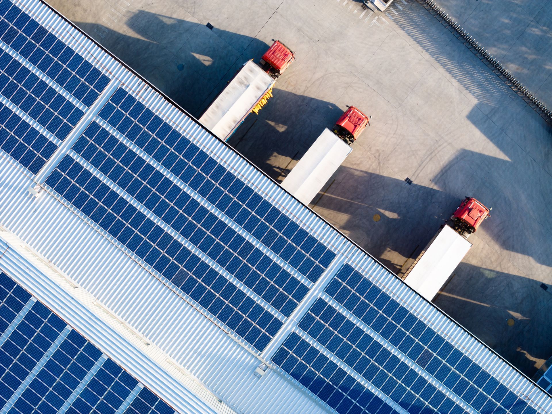 Vista dall'alto dei pannelli solari sul tetto di un magazzino con camion parcheggiati alle banchine di carico.
