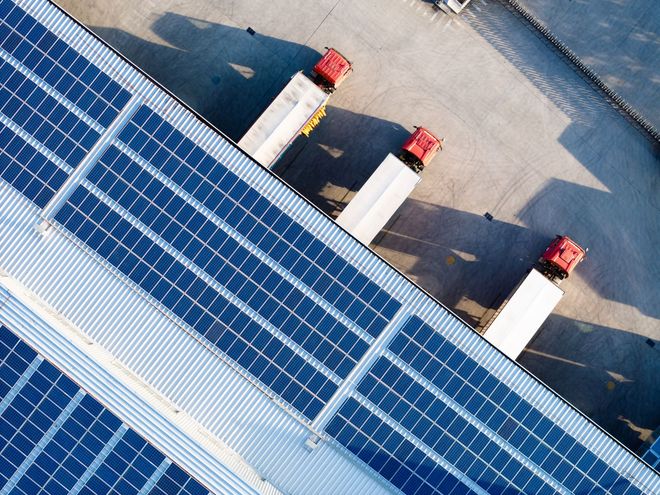 Vista dall'alto dei pannelli solari sul tetto di un magazzino con camion parcheggiati alle banchine di carico.