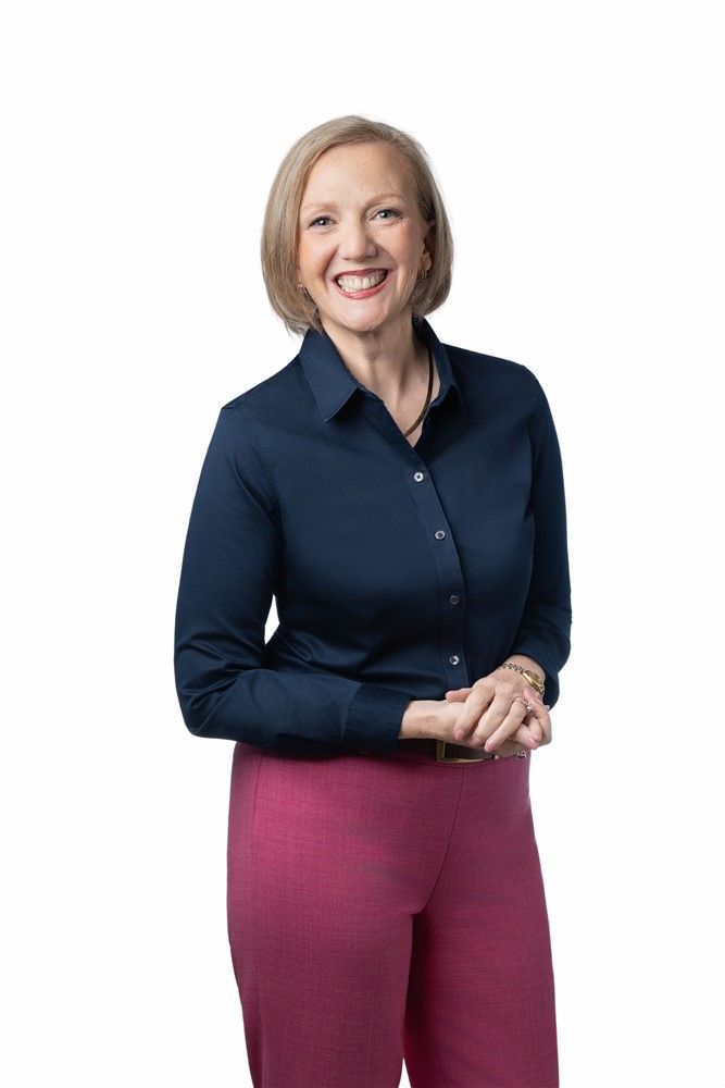 A woman wearing a green shirt and a black jacket smiles for the camera