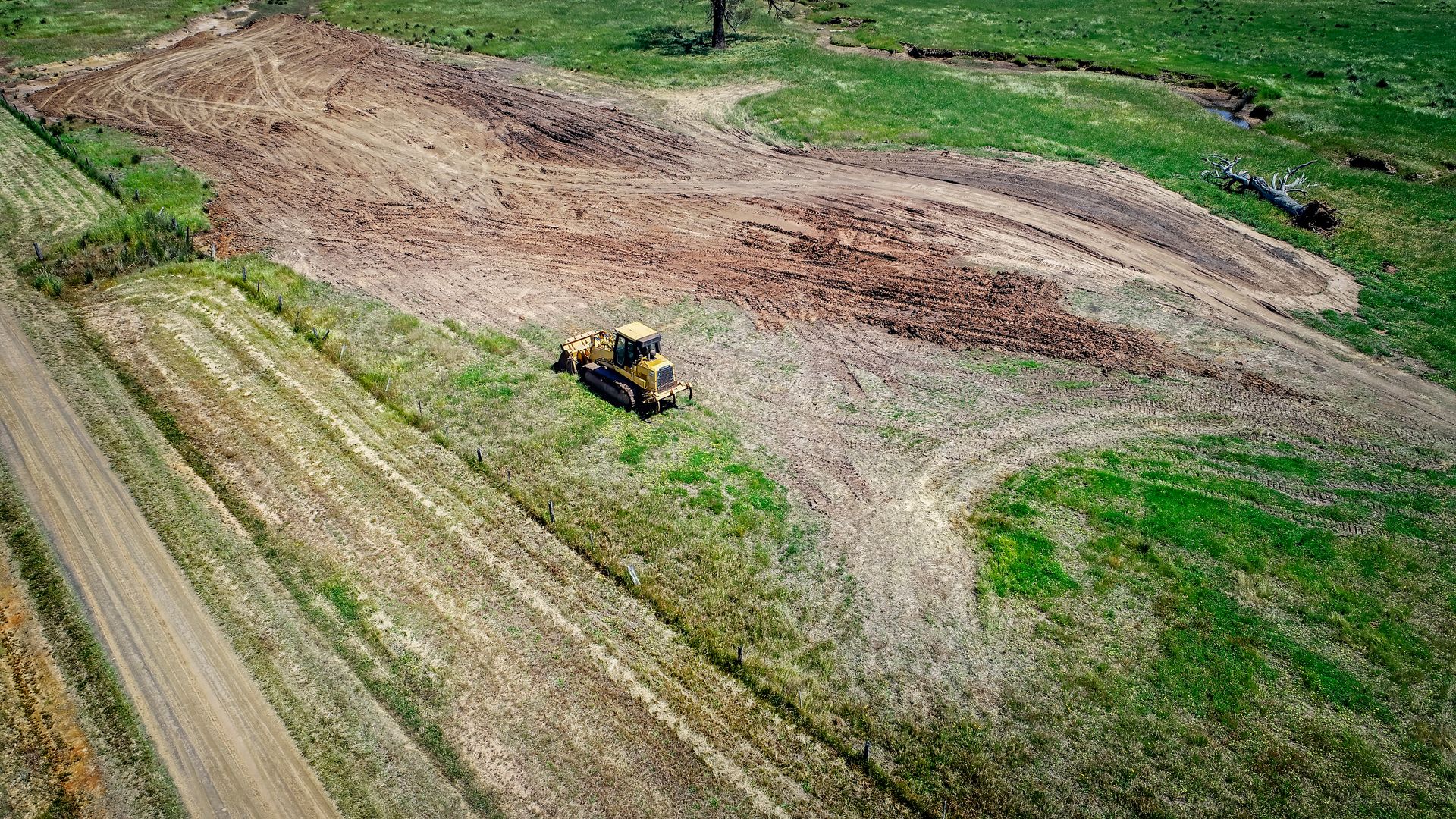 Bulldozer on a grassy hillside, clearing land near a field.