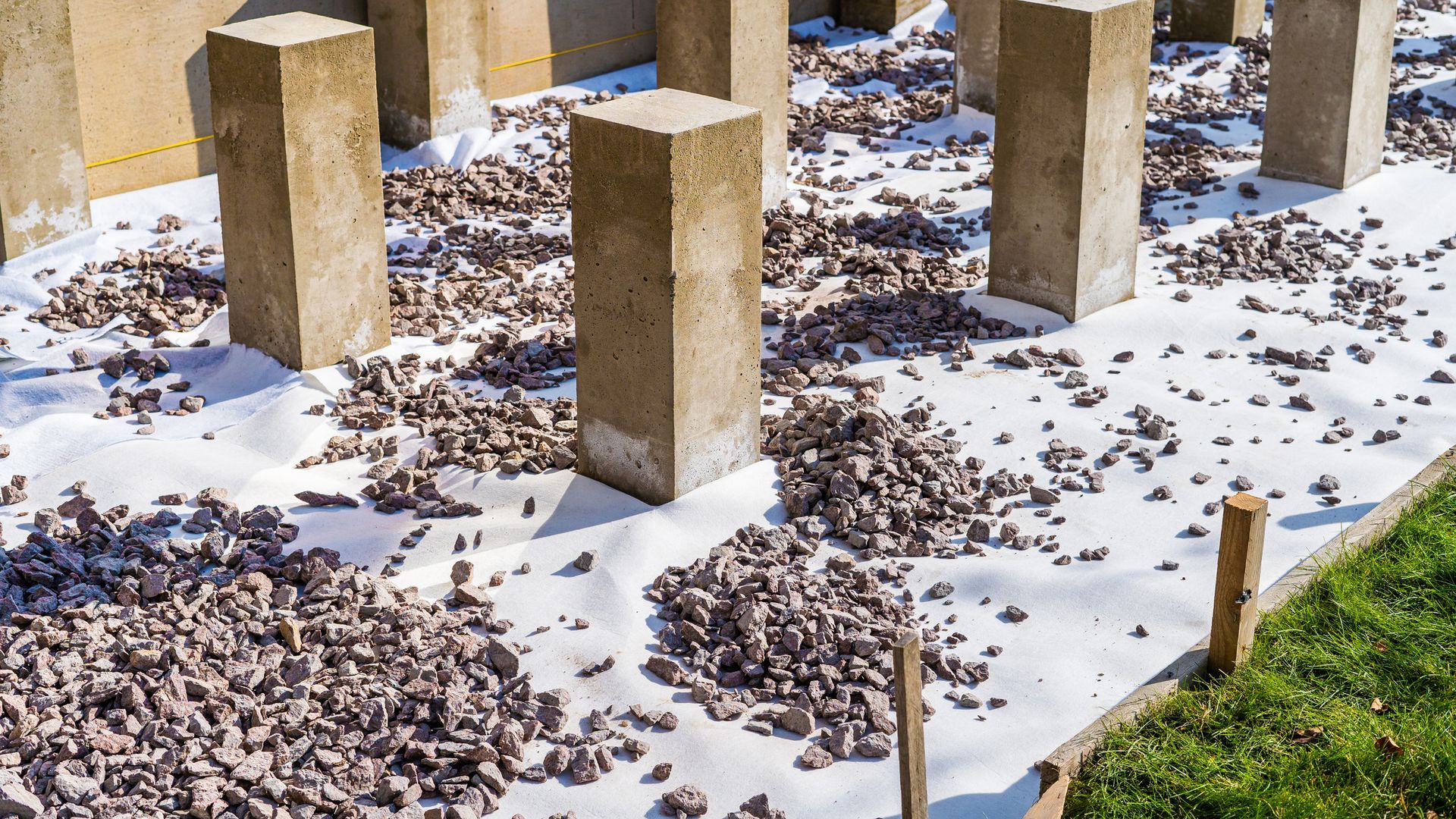 Concrete pillars on a white fabric covered base, with gravel surrounding them, outdoors.