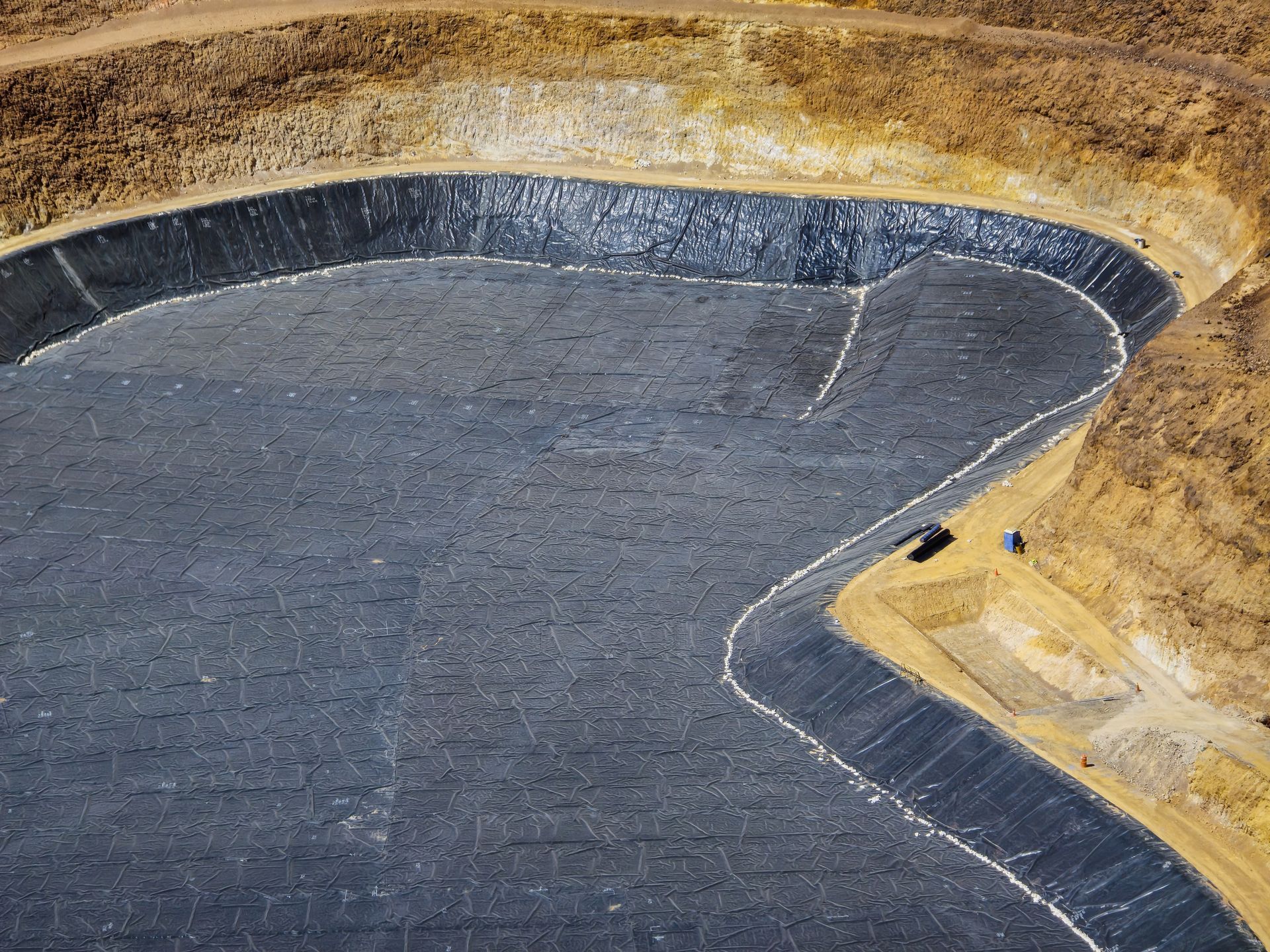 Large, black-lined reservoir dug into a hillside, likely for water containment, with brown earth surrounding.