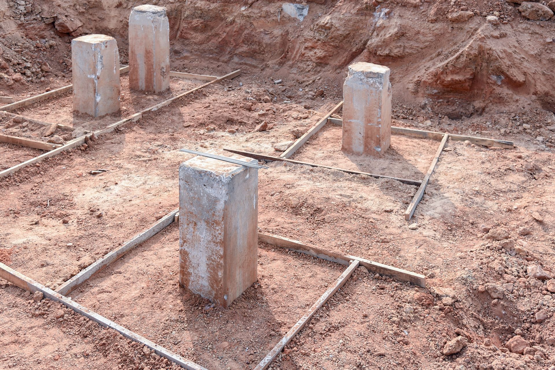 Concrete pillars and rebar framework in a construction site, set in reddish soil.