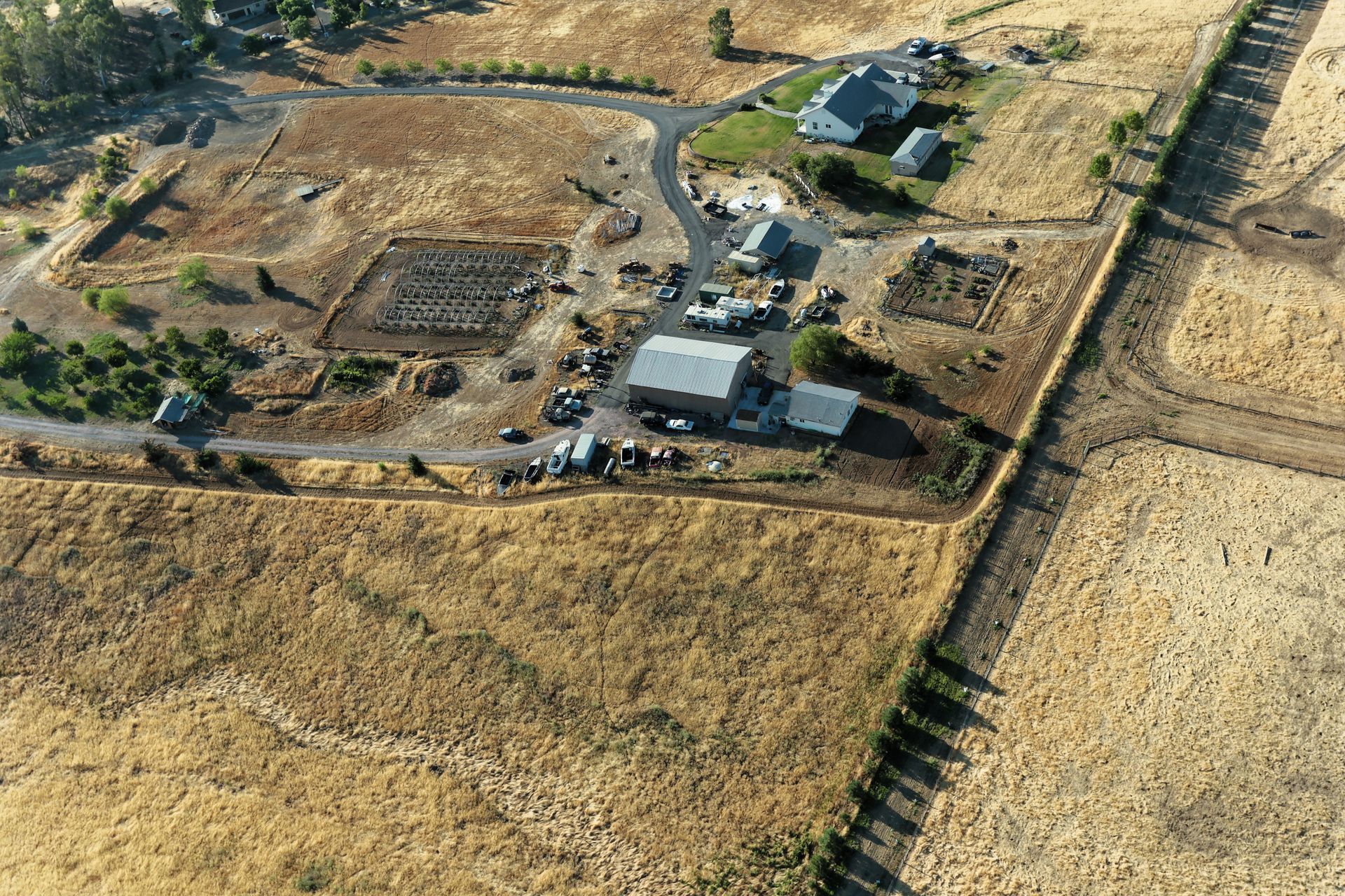 Aerial view of a farm with buildings, fields, and a road in a dry, grassy landscape.