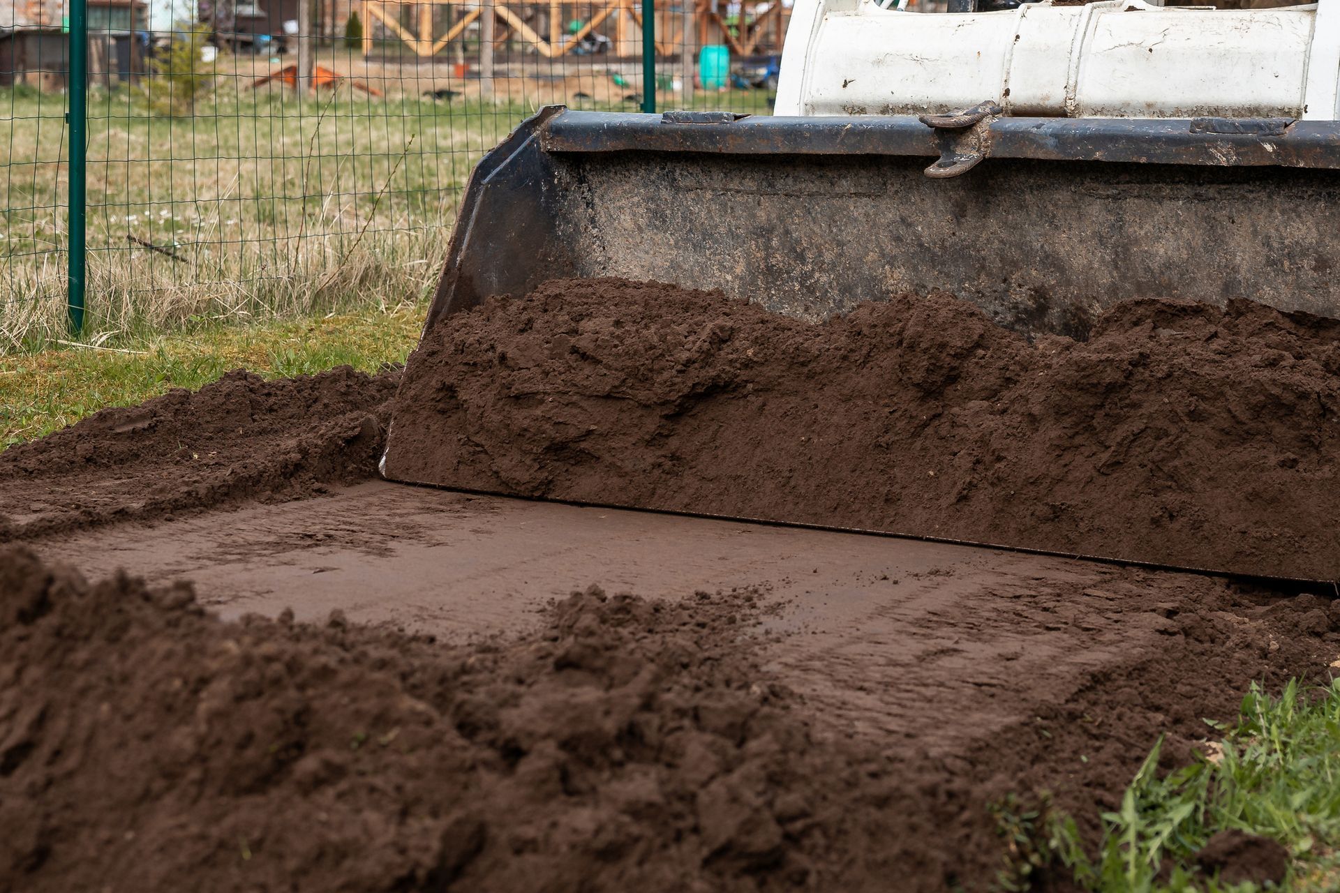 A front-end loader pushing a pile of dark brown soil on a grassy area.