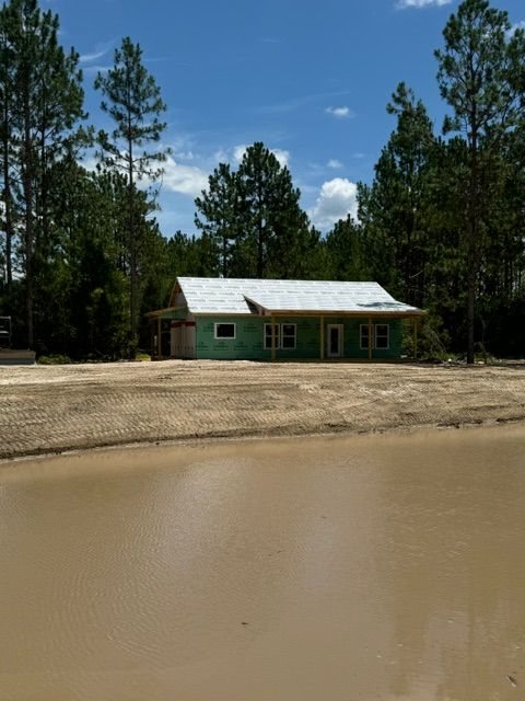 A new construction house with a light-colored roof surrounded by trees and a muddy area.