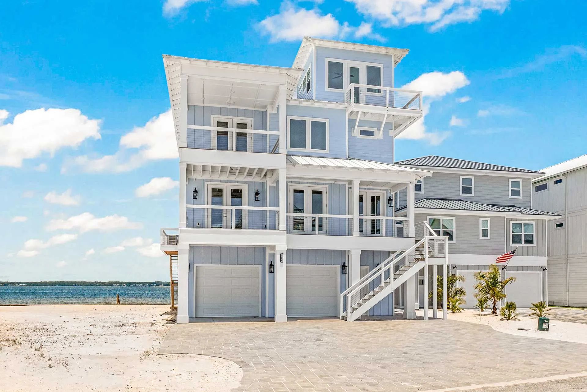 A large house is sitting on top of a sandy beach next to the ocean.