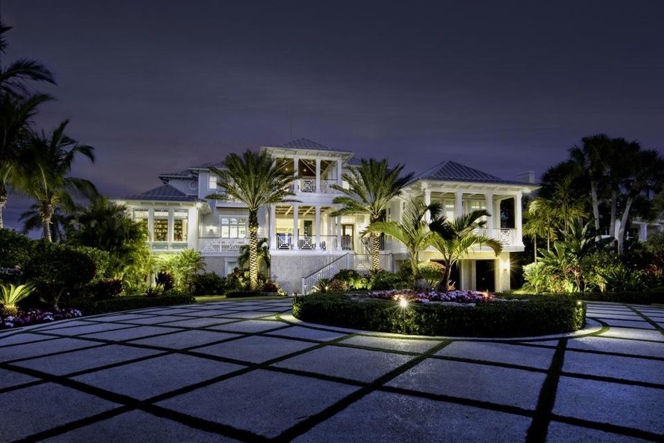 Luxurious white house at night with illuminated landscaping and paved driveway.