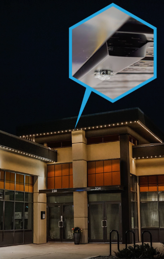 Exterior of a building at night. A detailed inset shows a close-up of a security camera mounted under an awning.