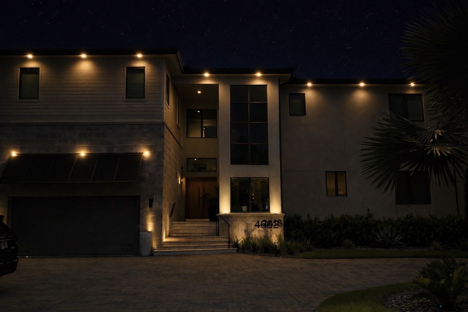 A two-story house at night, lit by exterior lights, with a starry sky in the background.