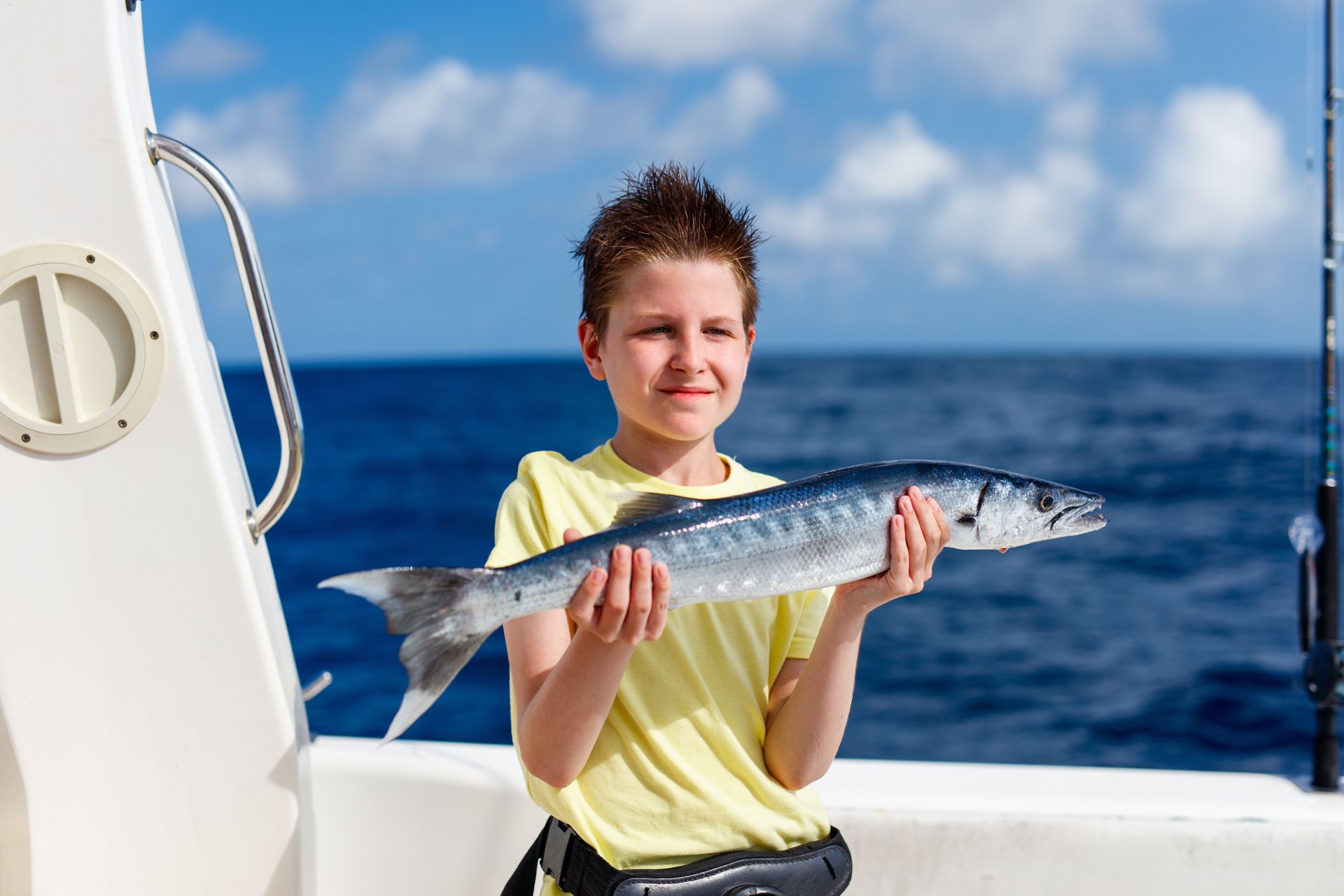 Boy holding a silver fish on a boat with the blue ocean in the background