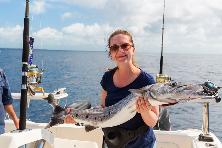 Woman holding a large fish on a boat with the ocean in the background