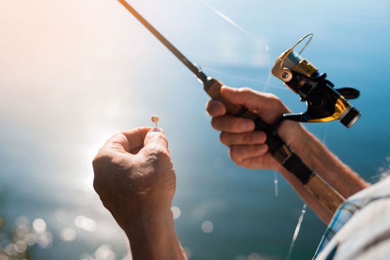 Hands holding a fishing rod and a small lure against a bright, blurred blue water background