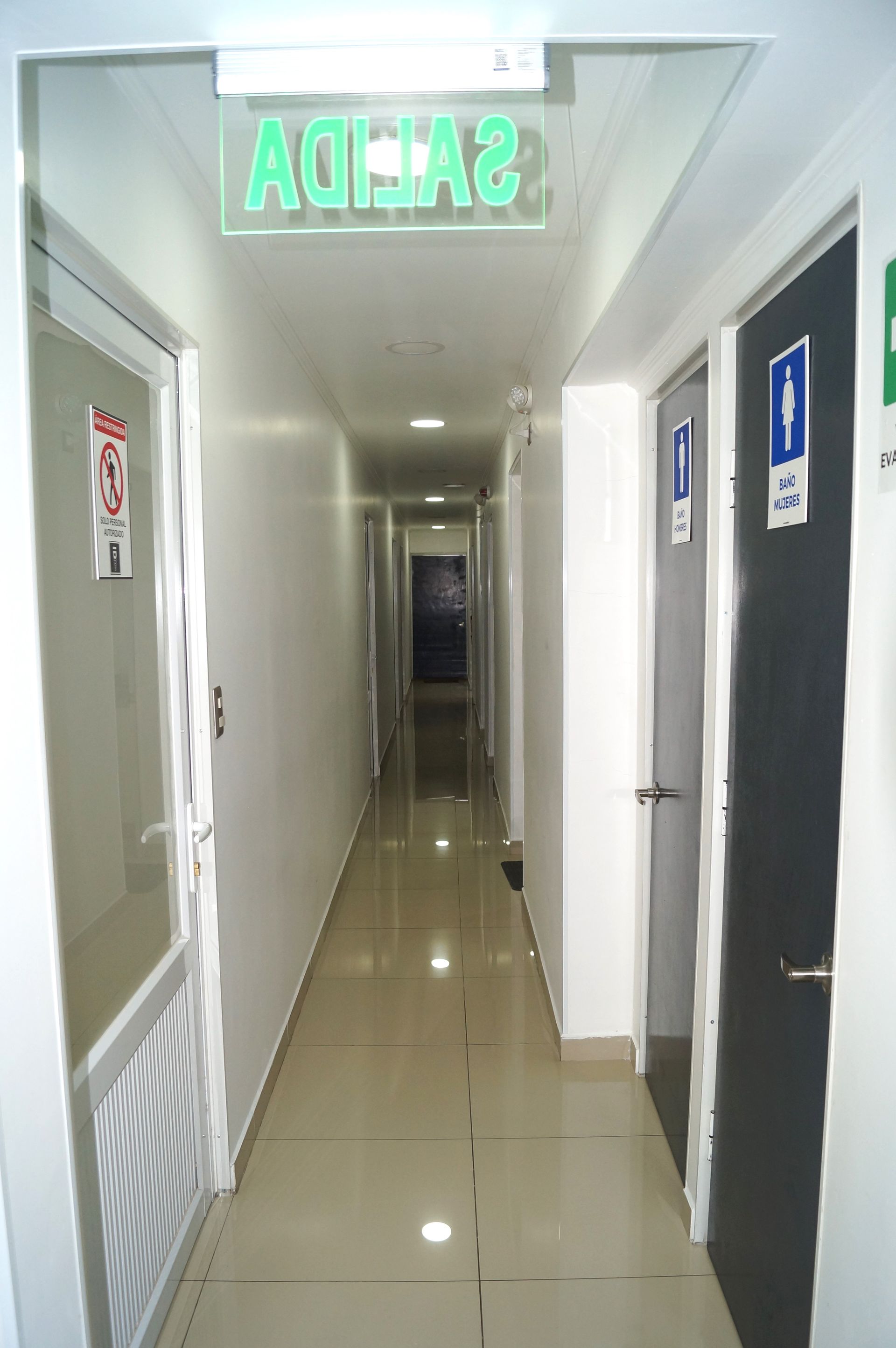 Un pasillo largo con una señal de salida verde encima.