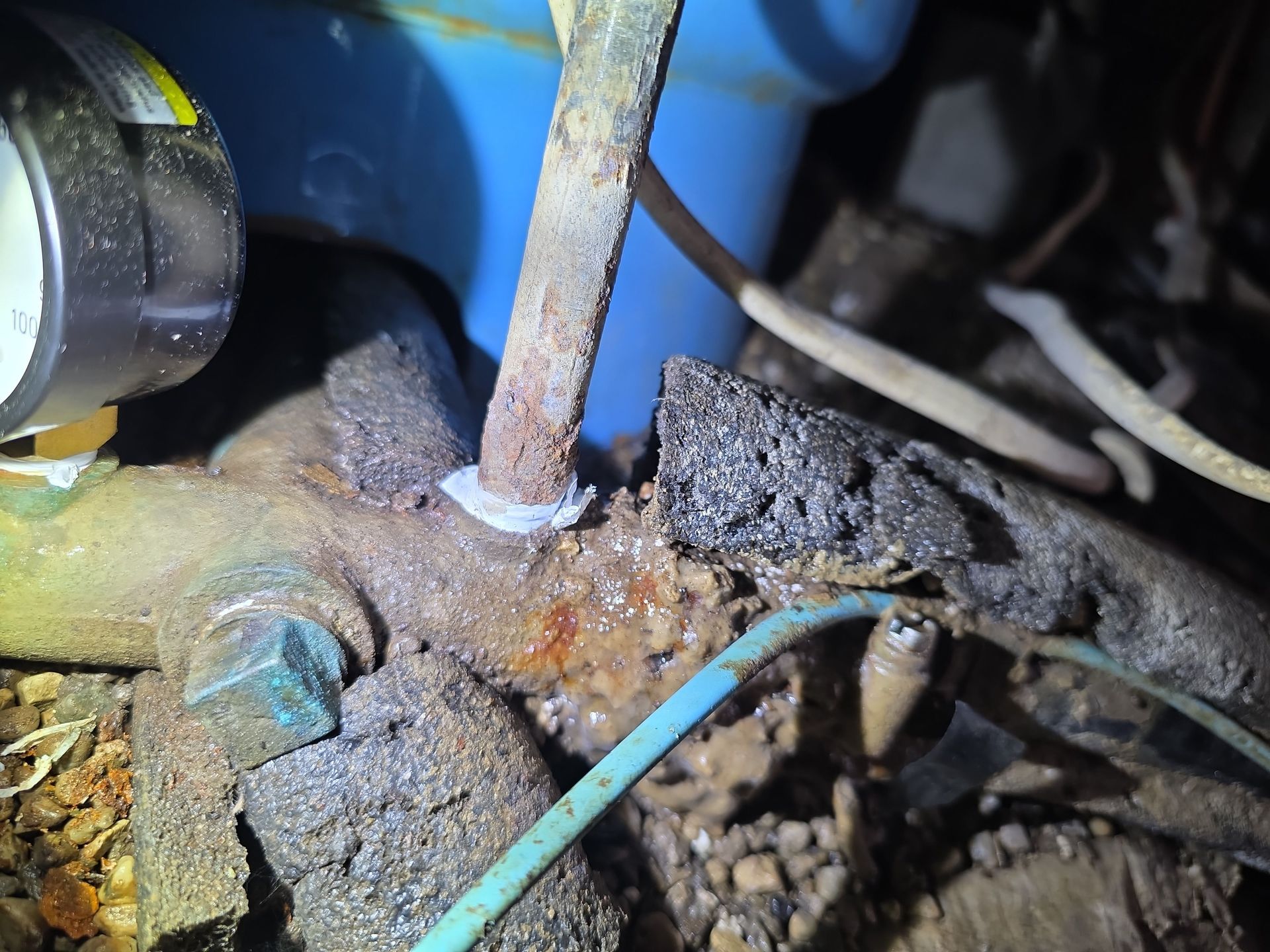 Close-up of corroded metal plumbing with exposed wires and a blue pipe in the background.