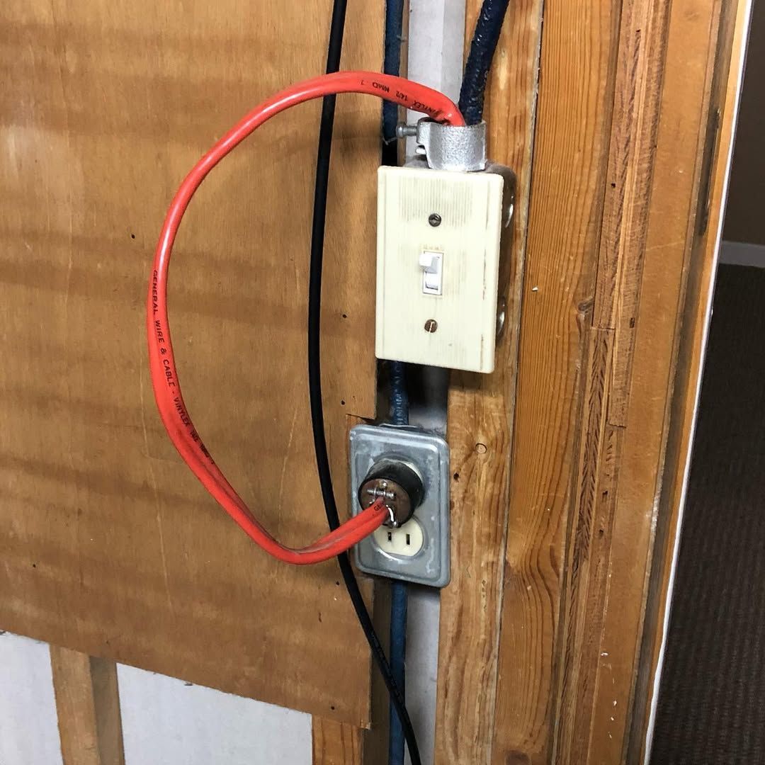 Electrical outlet and switch wired with a red cable, mounted on a wooden surface.