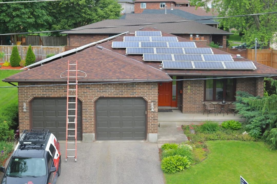House with brown roof and brick exterior, solar panels installed. A ladder leans against the roof. Black SUV parked.